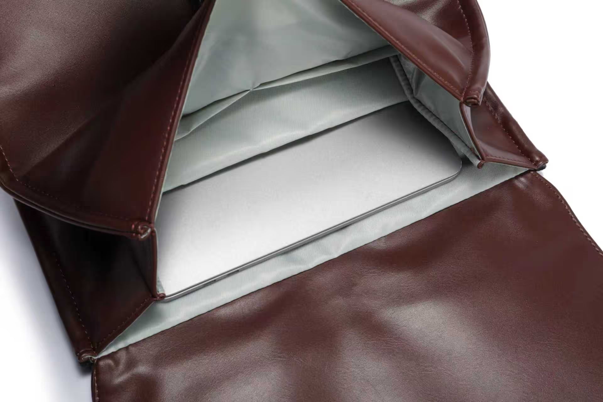 Ordinateur portable argenté placé à l'intérieur d'un sac en cuir marron ouvert, avec doublure grise.