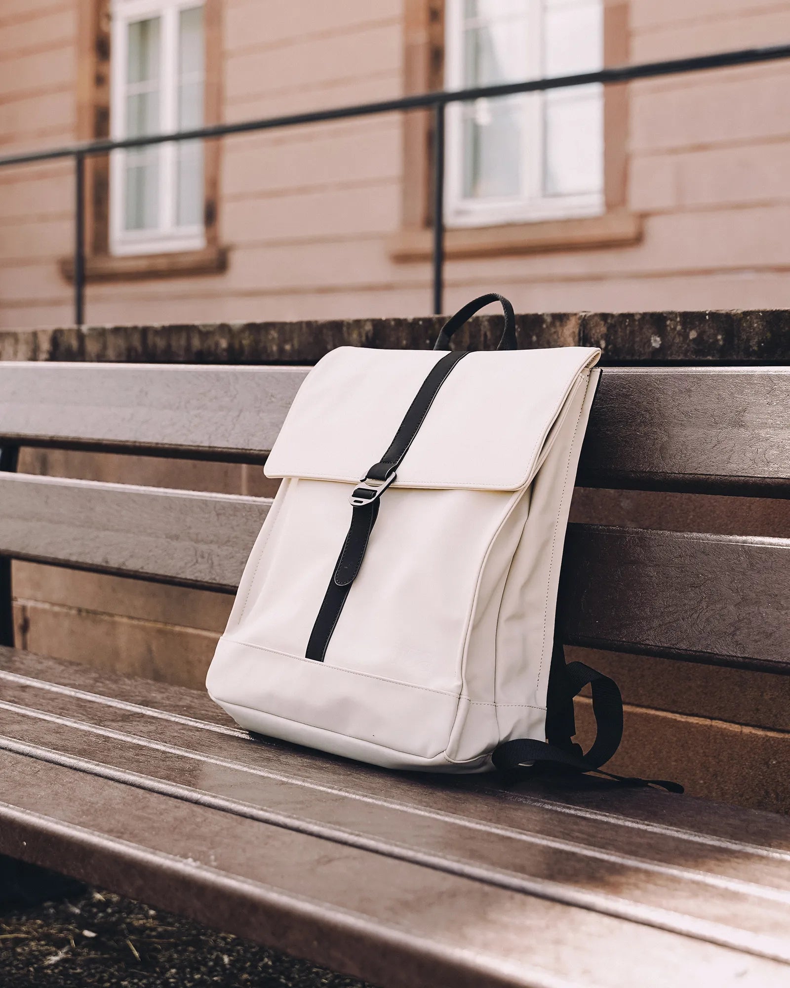 Sac à dos blanc avec une sangle noire posé sur un banc en bois marron à l'extérieur.