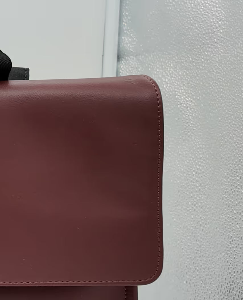 Sac à dos en cuir marron avec une couture visible sur un fond clair texturé.