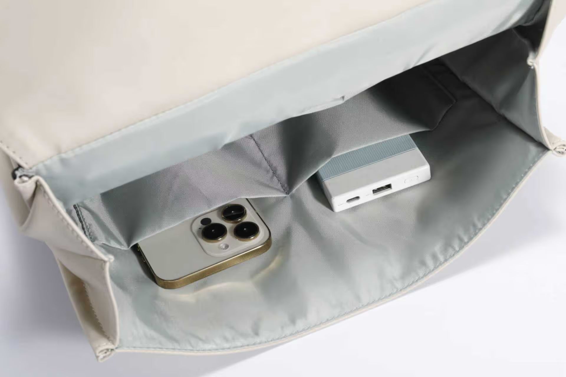 Intérieur d'un sac beige contenant un smartphone et une batterie externe.